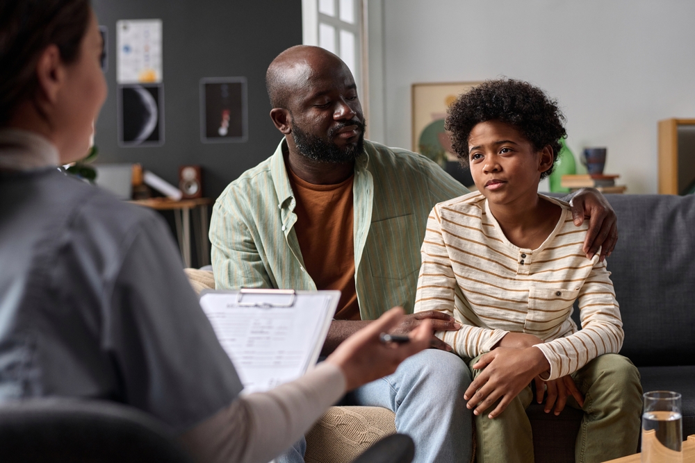 Father and child sitting on a sofa talking with a therapist.
